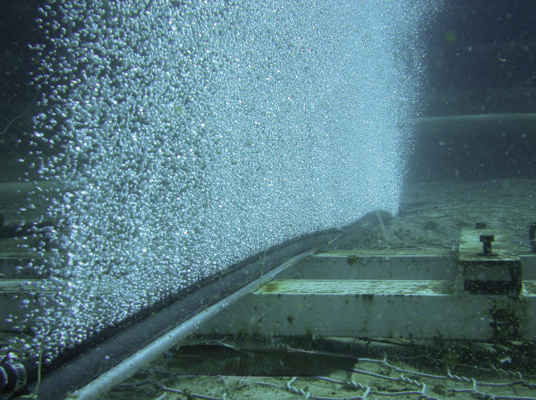 A subsea bubble curtain rising from a diffuser hose clamped to a frame above the seabed